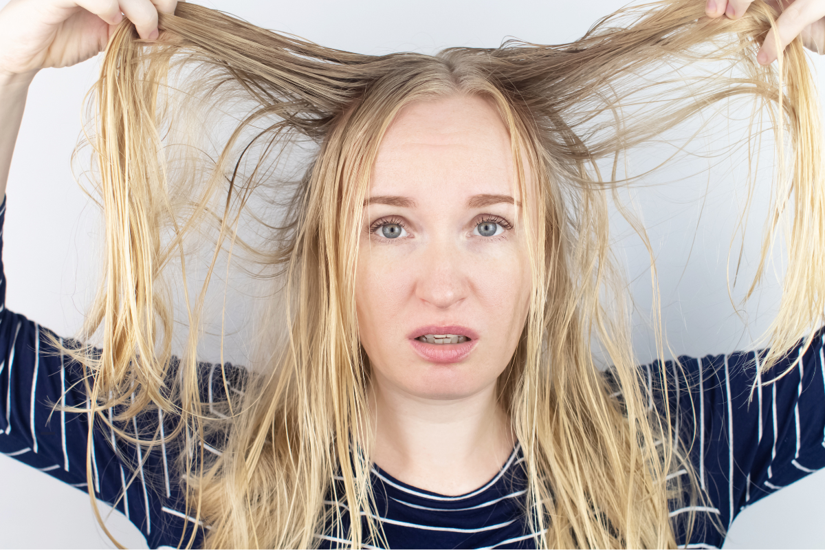 Mujer con el cabello graso y dañado, sujetando sus mechones con expresión preocupada, ilustrando la necesidad de un cuidado capilar adecuado con aceites vegetales reguladores.