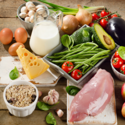 Fresh, healthy foods representing different diets: green vegetables, cherry tomatoes, avocado, eggs, cheese, milk, chicken, cereals and fruit, illustrating the influence of nutrition on the intestinal microbiota.