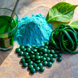 Spiruline en poudre, comprimés et boisson verte présentés sur une surface minérale, illustrant la spiruline disponible en pharmacie.